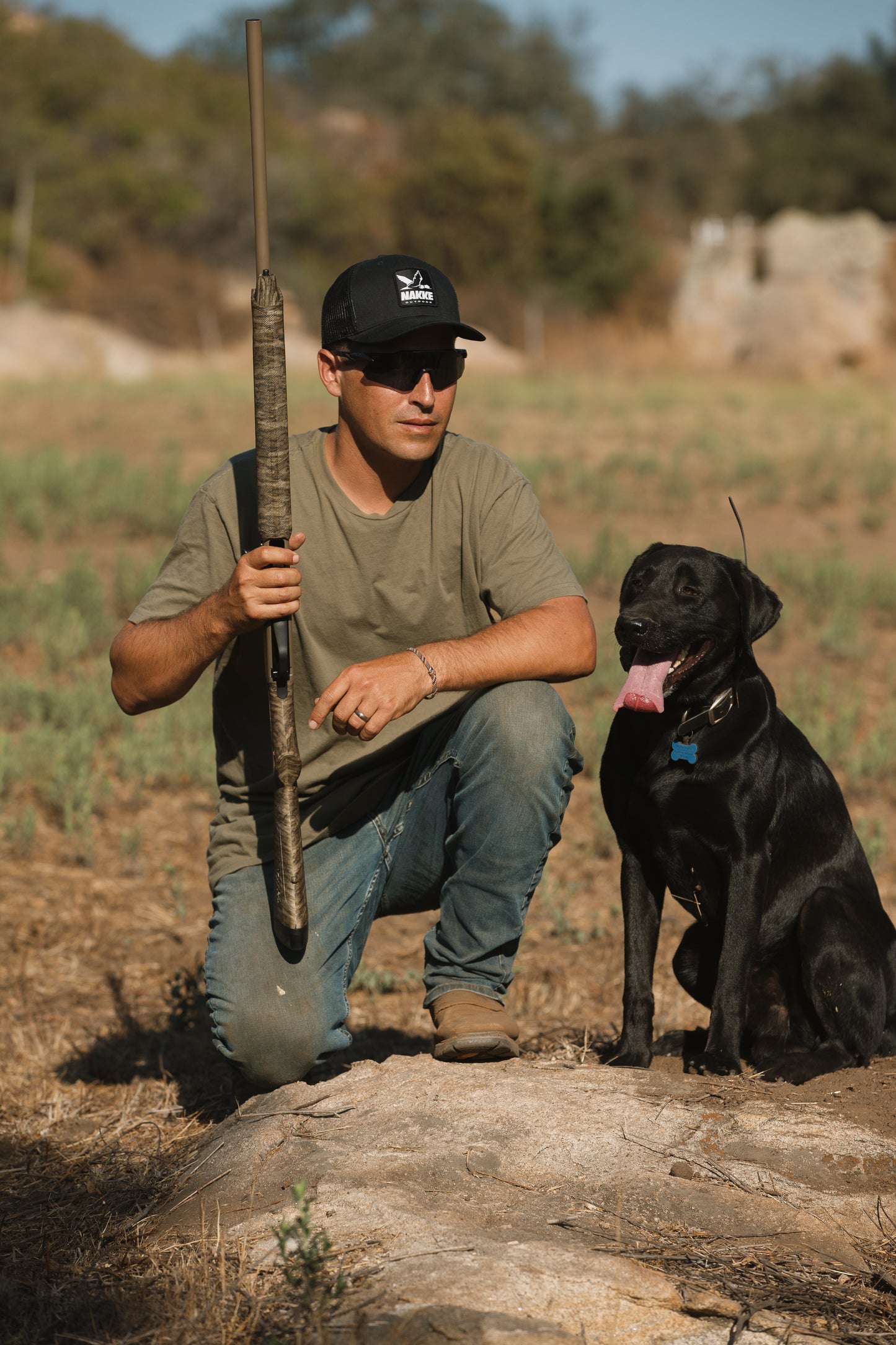 Man with black Labrador wearing the Black Mesh Back Trucker Hat with Nakke Drake Logo Patch