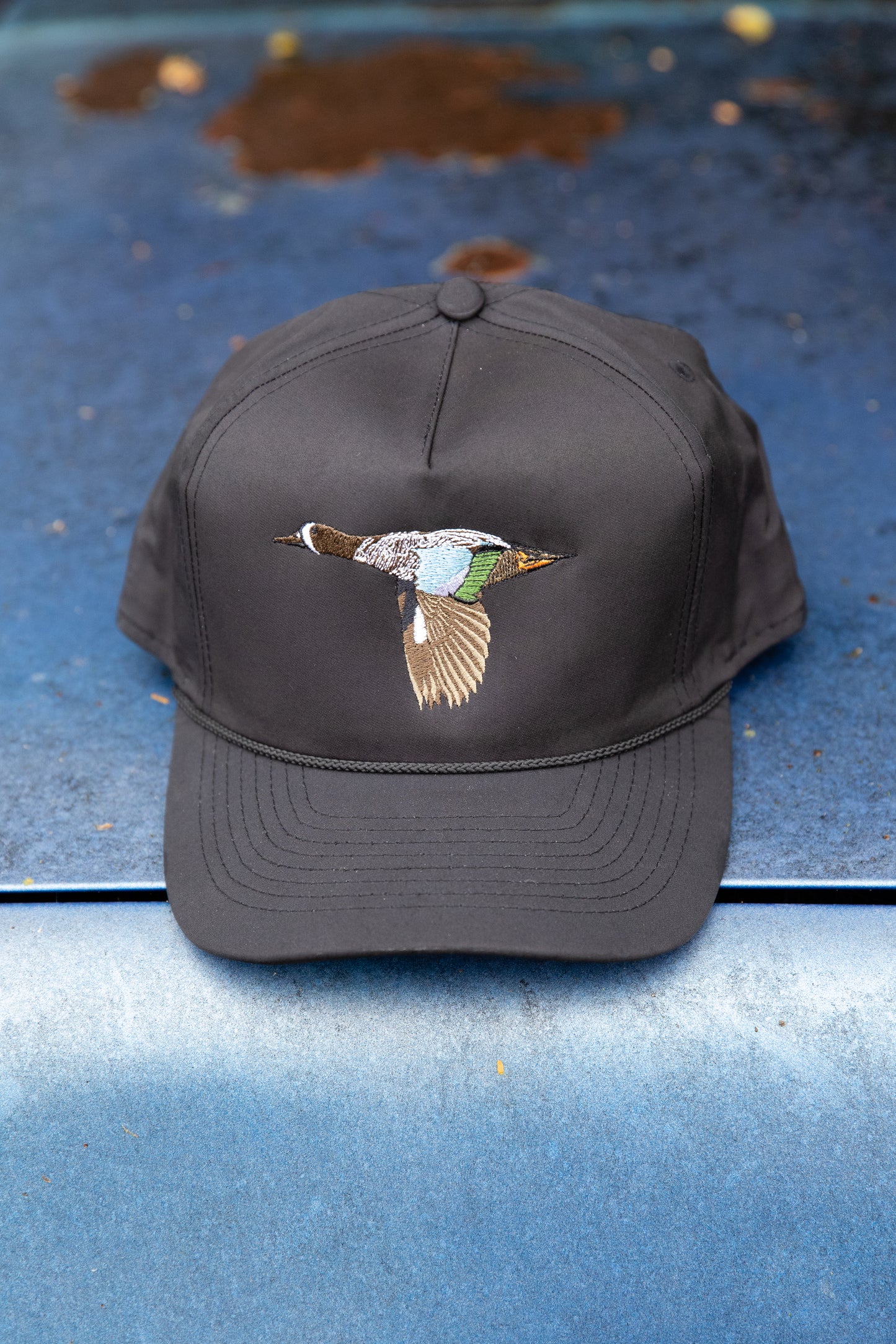 black hat with blue wing teal duck embroidered on the front and a black woven rope along the base